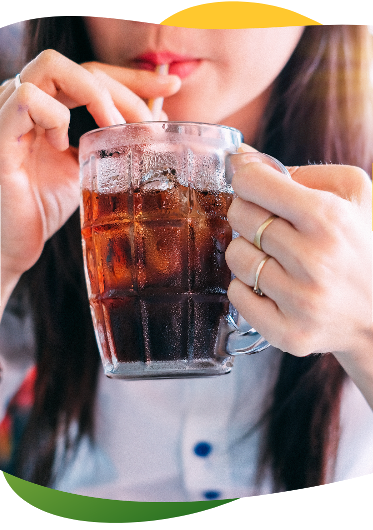 Jauna moteris ilgais rudais plaukais rankoje laiko aukštą stiklinę ir per šiaudelį geria gazuotą gėrimą.